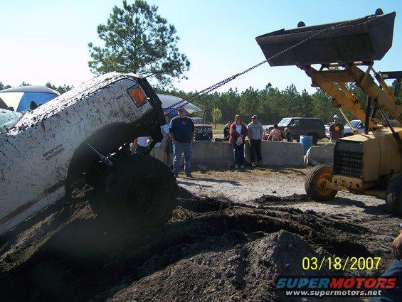 Mud-covered 1989 Ford Bronco tilted on its side, being pulled by a loader
