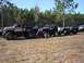 1989 Ford Bronco - Several off-road vehicles are lined up in a grassy field, with a modified pickup truck in the foreground.