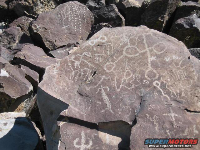 Petroglyphs etched into large rocks in a dry, rocky landscape