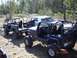 1989 Ford Bronco - Modified off-road vehicles are parked in a grassy, wooded area on a sunny day.