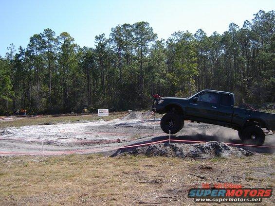 Dark green pickup truck with large tires driving off-road, kicking up dust