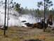 1989 Ford Bronco - A white pickup truck is obscured by smoke during an event, with a backhoe nearby and checkered flags strung overhead.