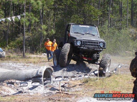 Dark off-road vehicle with large tires navigating a dirt obstacle course