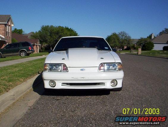 Front view of a white 1991 Ford Mustang with a raised hood, parked on a residential street