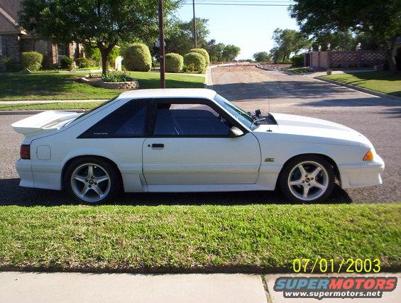 White 1991 Ford Mustang hatchback parked on a residential street, side view. Hood is slightly ajar