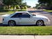 1991 Ford Mustang - A white 1991 Ford Mustang hatchback is parked on the side of a suburban street on a sunny day.