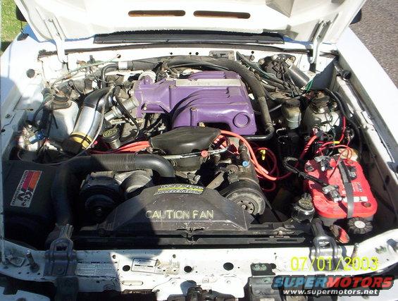 1991 Ford Mustang engine bay with purple valve covers and a red battery