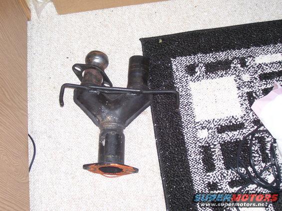 Black metal exhaust manifold with two pipes merging into one, resting on a carpet
