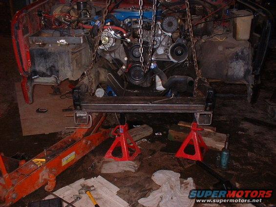 Red truck engine bay with engine suspended by chains, supported by jack stands