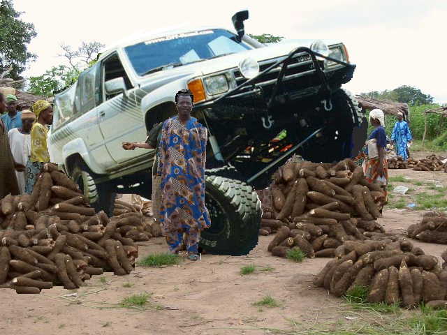 Modified Toyota pickup truck with large tires and a snorkel, parked next to piles of root vegetables and people