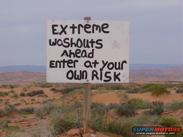 Sign warning 'Extreme Washouts Ahead Enter at your Own Risk' in a desert landscape