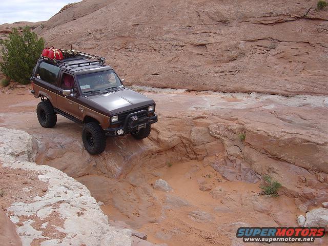 1986 Ford Bronco II with roof rack and jerry cans navigating rocky terrain