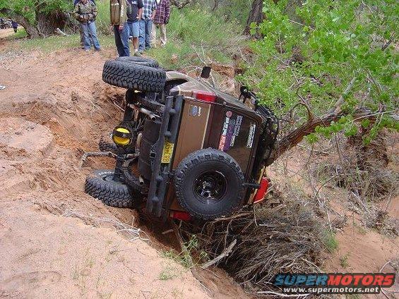 1986 Ford Bronco II overturned on its side in a sandy ditch with people watching