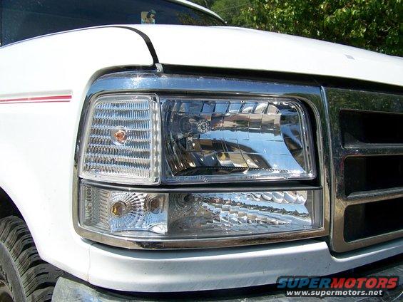 White Ford truck front corner with chrome grille and rectangular headlight assembly. Red stripe on fender