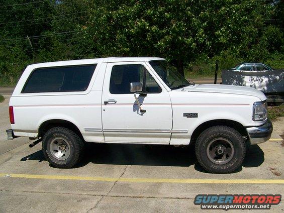 Side view of a white 1995 Ford Bronco parked on pavement with trees in the background