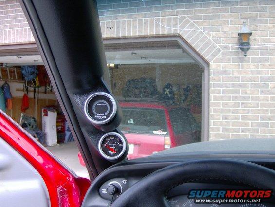 interior shot of air/fuel and transmission temperature gauges mounted on a pillar, red vehicle door visible, garage with red truck in background