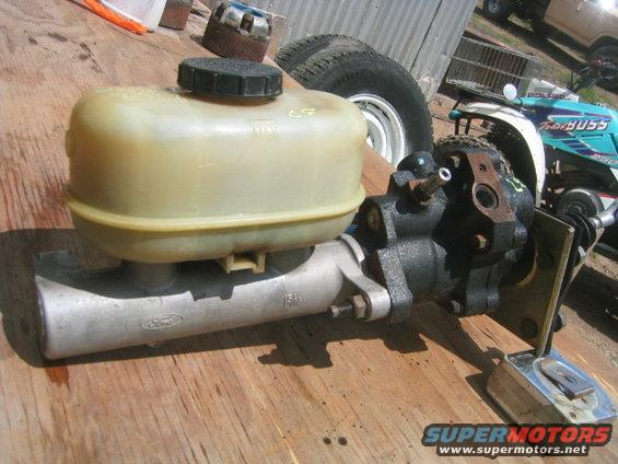 Ford master cylinder with plastic reservoir and cap, mounted on a wooden surface. Part number visible