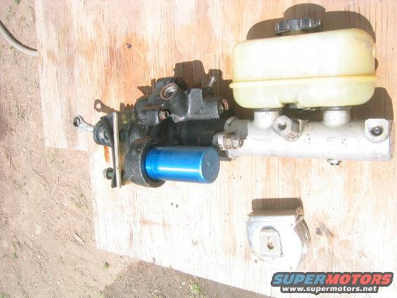 Brake master cylinder and booster assembly with a blue accent cylinder, resting on a wooden surface