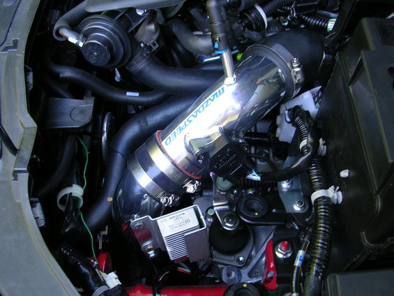 Engine bay with shiny metal Mazdaspeed intake tube and various hoses and wires