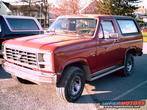 Red Ford Bronco with a black top, parked next to another Bronco