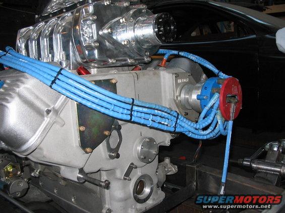 Close-up of a supercharger mounted on an engine block with blue spark plug wires
