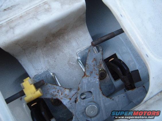 Tailgate latch mechanism with rusted metal parts and a yellow plastic clip