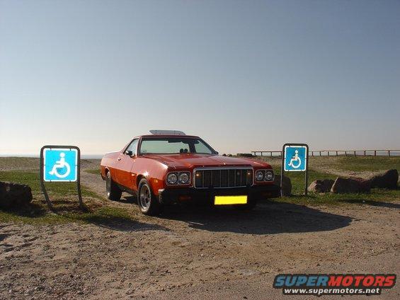 Orange 1974 Ford Ranchero parked near a beach with two handicap parking signs