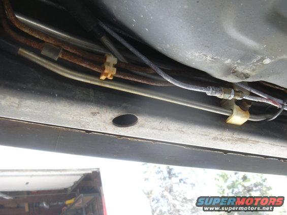 Underbody view of rusted brake lines and fuel lines secured by yellow clips to a metal frame
