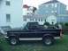 1993 Ford Bronco - This black Ford Bronco is parked on a grassy lawn in front of residential buildings.