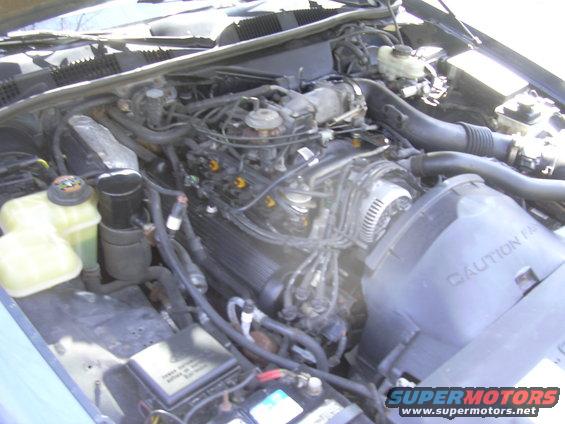 Engine bay with V8 engine, coolant reservoirs, and fan shroud with caution text