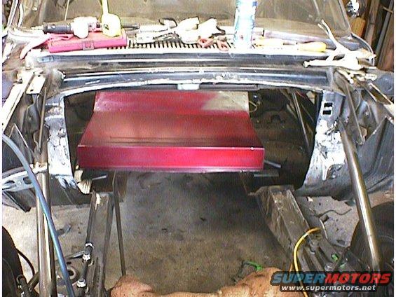 Car engine bay with red metal piece installed, tools on dashboard