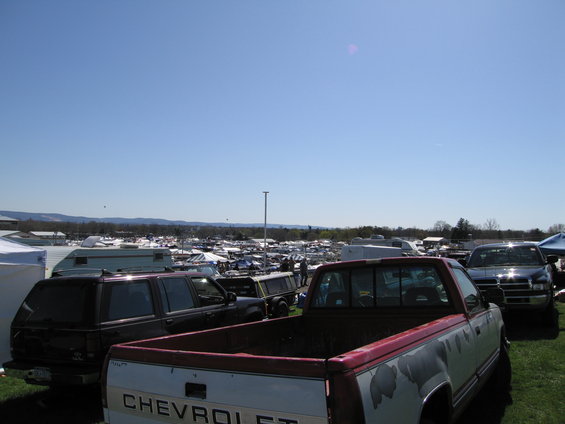 Truck bed with peeling paint, parked next to a dark SUV and other vehicles at an outdoor market