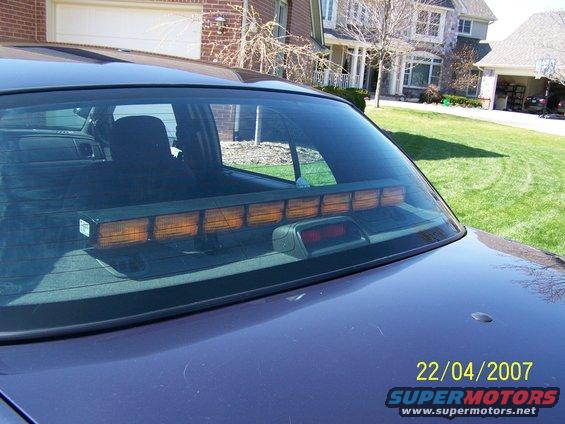 Dark blue car's rear window with an amber light bar and a red brake light visible
