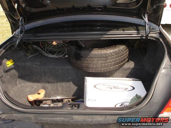 Trunk of a car with a spare tire, a box labeled 'Eagle', and some wiring