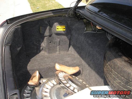 Car trunk interior with spare tire, hubcaps, and two tan shoes