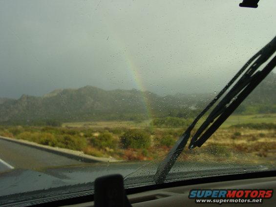 View through a wet windshield at a rainbow over mountains