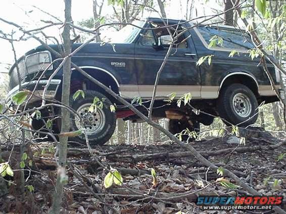 1993 Ford Bronco driving over logs and branches in a wooded area