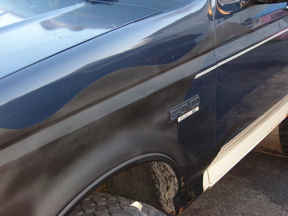 Side view of a 1993 Ford Bronco with a dark blue body and a cream-colored lower trim. The 'BRONCO' badge is visible on the fender