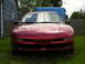 1996 Ford Probe - The front end of a red 1996 Ford Probe is visible, parked outside a house with a wooden fence in the background.