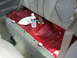1996 Ford Probe - The interior rear floor of a vehicle shows exposed red metal and gray carpet, with a water bottle and bag on the floor.
