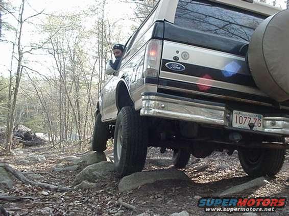 Ford Bronco driving over rocks off-road, driver visible in window