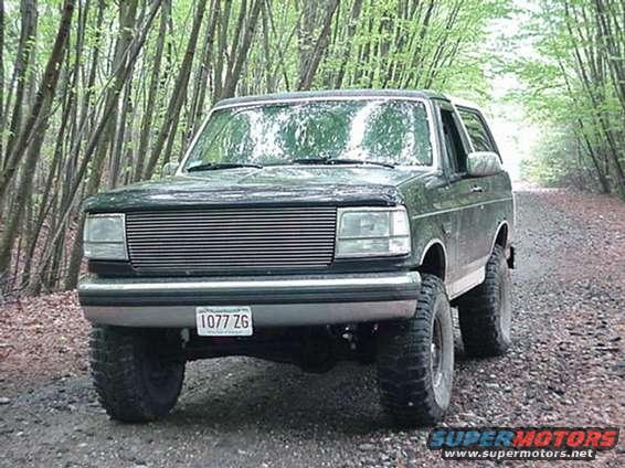 Dark green Ford Bronco parked on a dirt road with trees on both sides. License plate reads 1077 ZG