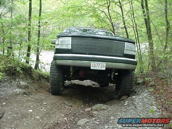 Black Ford Bronco on a dirt trail, front view. Lifted suspension, off-road tires, and a grille from the early 1990s
