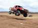 1992 Ford Explorer - A red off-road truck soars through the air during a jump, with another vehicle visible in the distance.