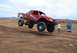 1992 Ford Explorer - A red off-road truck is airborne over a dirt ramp during a race.
