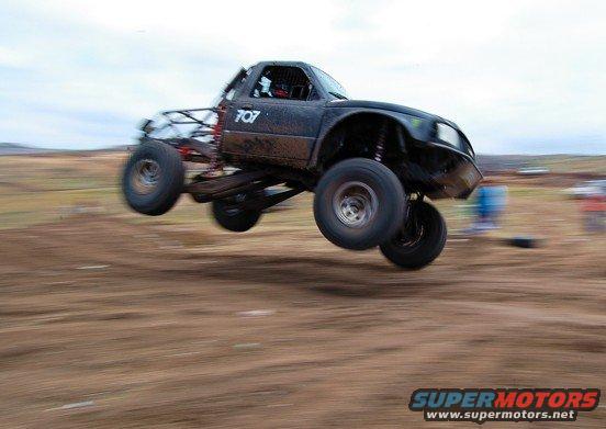 Black off-road truck with number 707 airborne over dirt track
