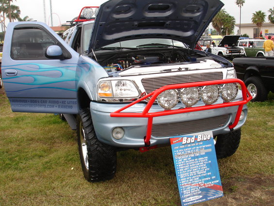Light blue pickup truck with flames, red bull bar, and hood open. Sign in front