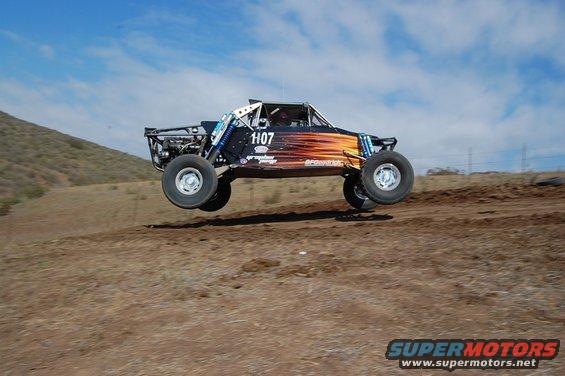 Off-road buggy with number 1107 airborne over dirt terrain, orange flame graphics on side