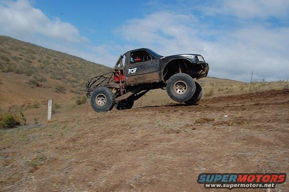 Off-road truck with number 707 on door, jumping over dirt terrain
