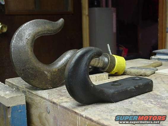 Two metal tow hooks, one large and rusty, the other black with a yellow cap on a bolt